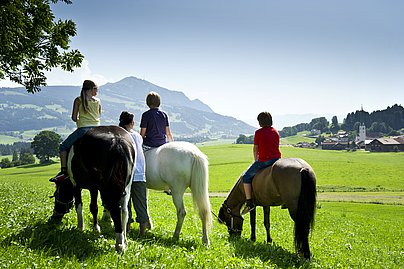 Drei Kinder sitzen auf Pferden und genießen den Ausblick auf den Grünten.