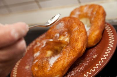 Drei Funkenküchle werden mit einem Löffel mit Zucker bestreut.