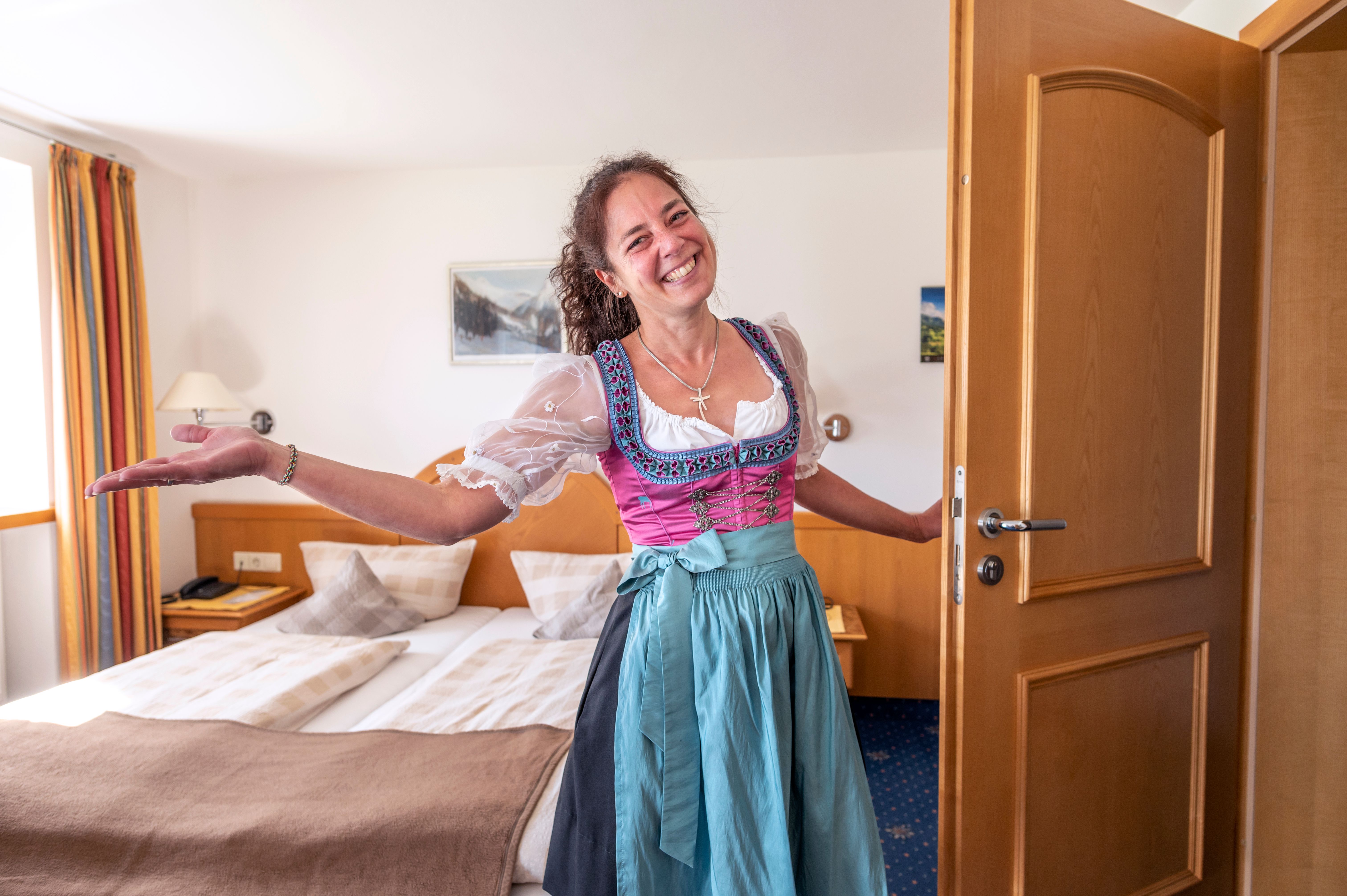 Eine Gastgeberin in Tracht begrüßt ihre Gäste herzlich in einem Ihrer Zimmer.