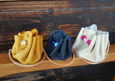 Drei kleine Handtaschen in verschiedenen Farben stehen auf einem Holzregal. Die Taschen sind gelb, navy und cremefarben und haben bunte Details.