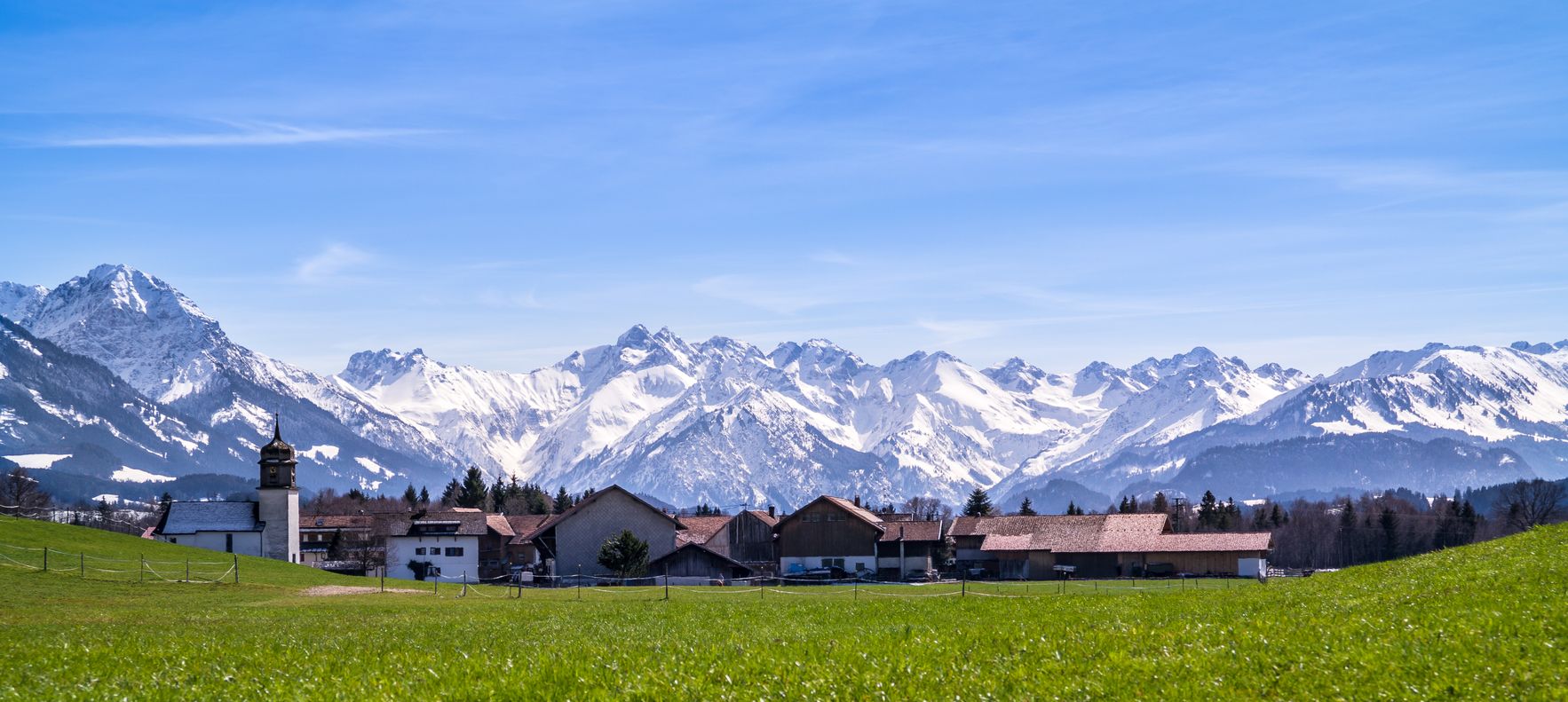 Der Burgberger Agathazell im Frühling. Im Hintergrund sind noch die schneebedeckten Allgäuer Hochalpen sichtbar.