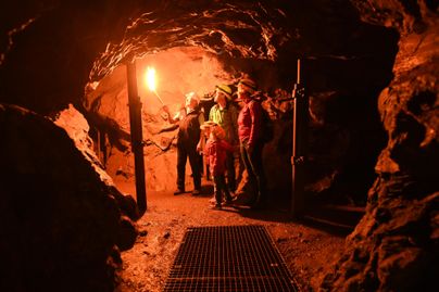 Eine Gruppe von Menschen steht in einer Höhle. Sie halten Fackeln und betrachten die Umgebung.
