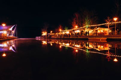 Der Große Alpsee bei Immenstadt bei Nacht mit beleuchteter Seebuehne und beleuchteten Ständen der Seeweihnacht.