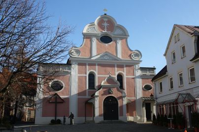 Eine schöne, rosa gefärbte Kirche mit aufwendiger Architektur. Der klare Himmel und die umliegenden Gebäude ergänzen die malerische Atmosphäre.