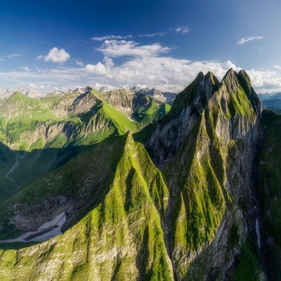 Eine Gruppe von Sängern steht auf einer grünen Wiese. Sie tragen bunte Oberteile in verschiedenen Farben und lächeln in die Kamera.