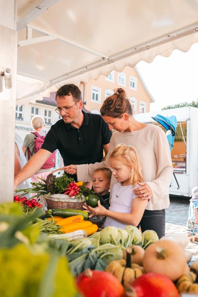 Eine Familie kauft frisches Gemüse auf einem Markt. Kinder helfen bei der Auswahl von buntem Obst und Gemüse.
