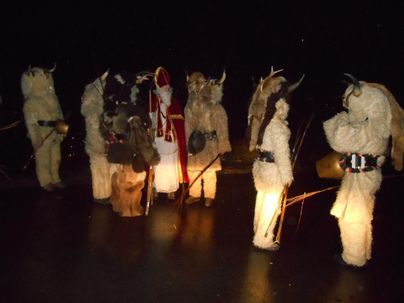 Eine Gruppe von Menschen in traditionellen Kostümen steht in der Dunkelheit. Sie tragen Felle und Accessoires und halten Stäbe in der Hand.