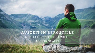 Ein Mann sitzt in meditativer Haltung auf einer Alpe und blickt auf die beeindruckenden Berge. Die Landschaft strahlt Ruhe und Frieden aus.