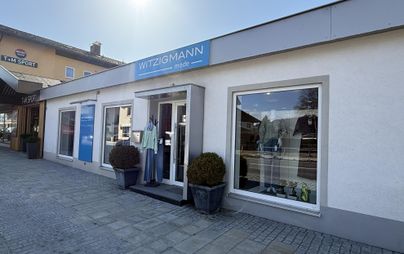 Ein Geschäft mit dem Namen "Witzigmann" an einer Stadtstraße. Die Fassade ist hell und hat große Fenster, die verschiedene Kleidungsstücke zeigen.