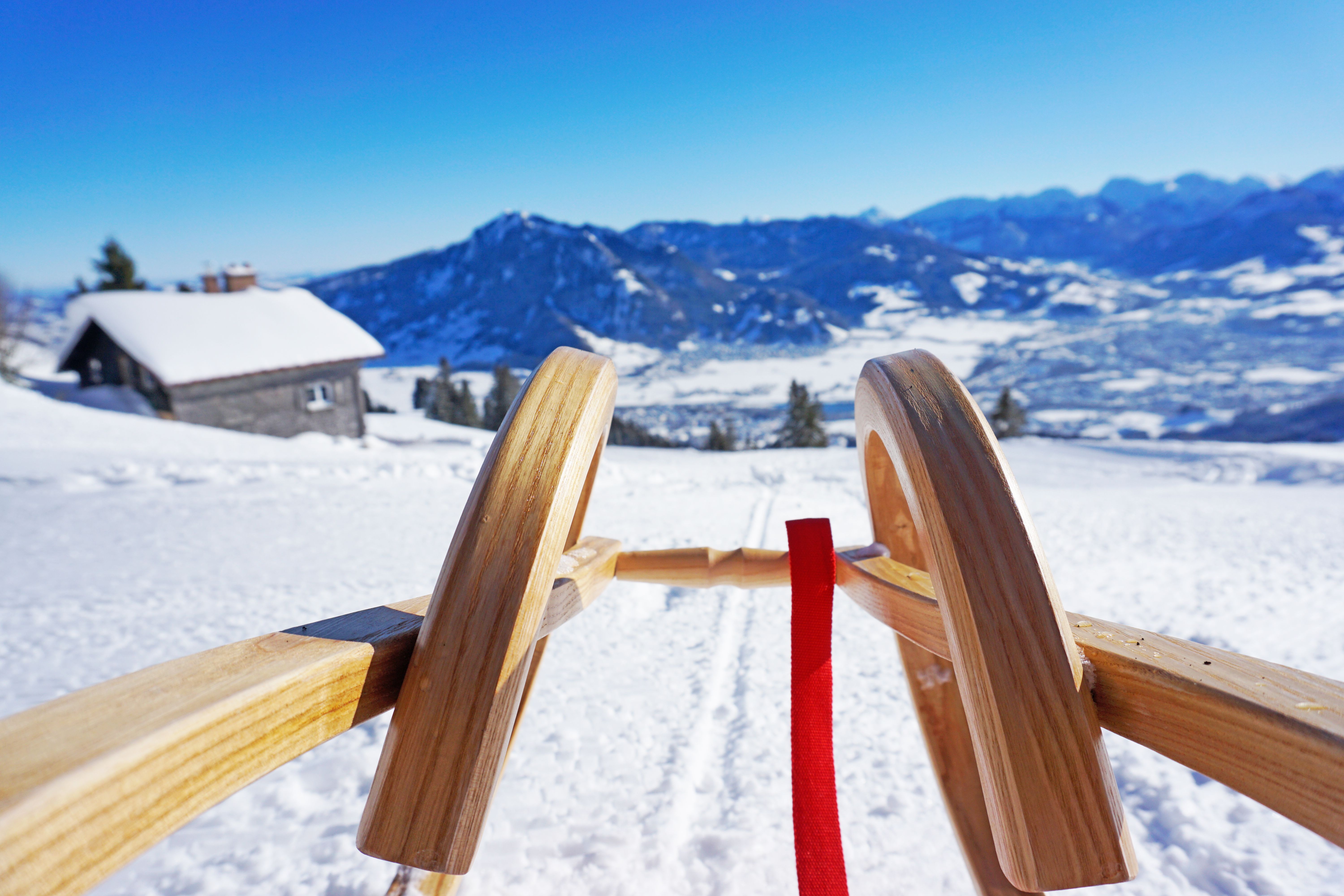 Ein Rodel fährt im Schnee bergab. Im Hintergrund ist der Grünten zu sehen. Die Naturrodelbahn vom Mittag Gipfel ist 5,2 km lang.