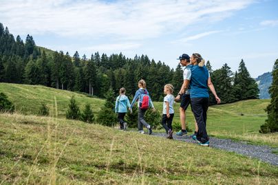 Eine Familie geht gemeinsam auf einem Weg in den Bergen. Es ist ein sonniger Tag und die Kinder haben Spaß.