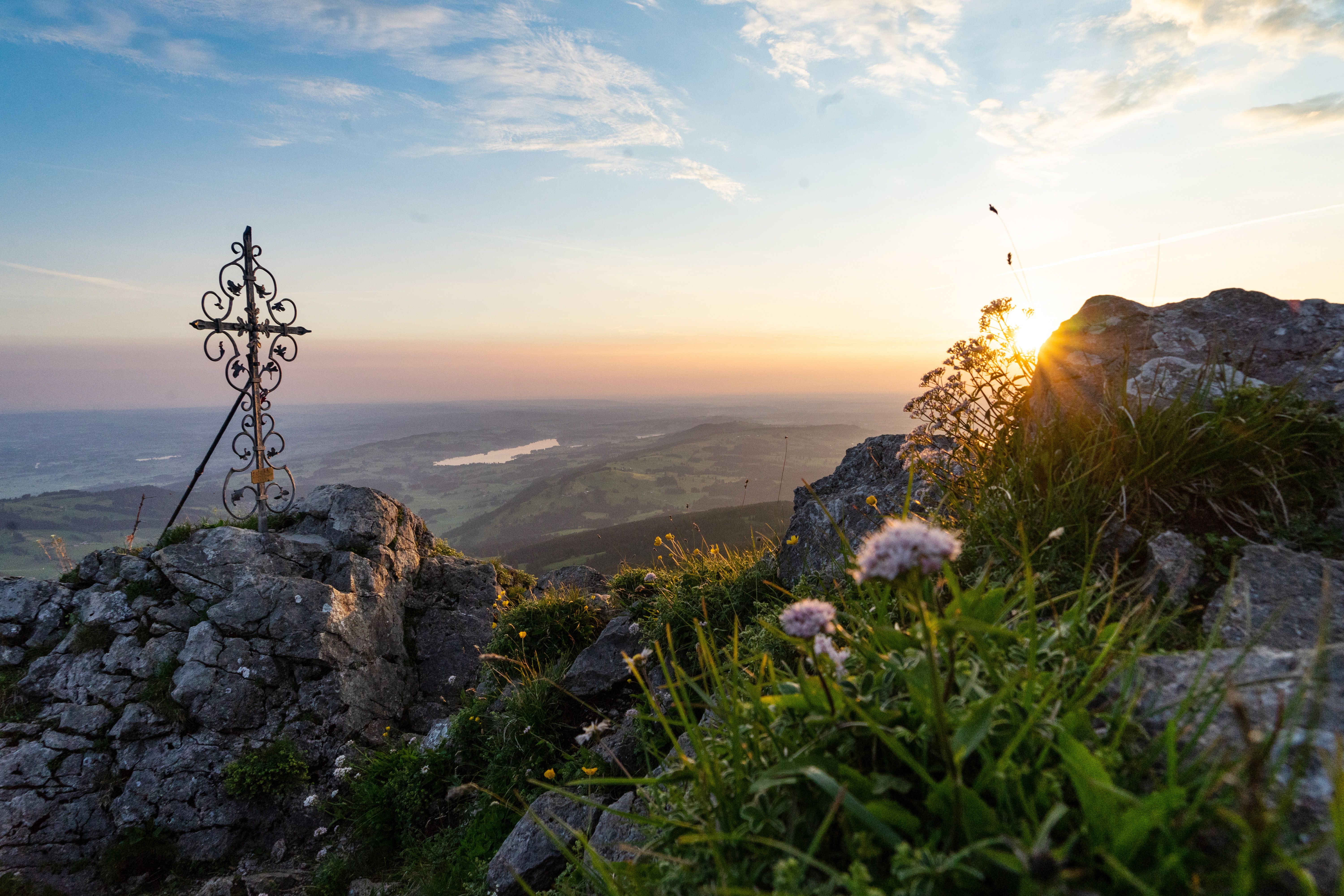 Hinter dem schmiedeeisernen Kreuz am Grüntengipfel geht die Sonne unter. Der Grünten, auch  "Der Wächter des Allgäus" genannt, ist ein 1.738 Meter hoher Berg. Schon von weitem kündigt er durch seine vorgelagerte Stellung den Einstieg in die Allgäuer Alpen an.