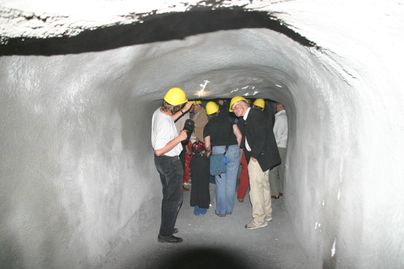 Eine Gruppe von Menschen steht in einem Tunnel und trägt gelbe Sicherheitshelme. Sie scheinen interessiert an ihrer Umgebung zu sein und untersuchen die Wände.