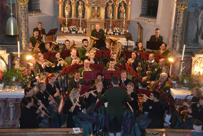 Ein Orchester spielt in einer Kirche. Die Musiker sind in festlicher Kleidung und umgeben von einer schönen dekorativen Kulisse.