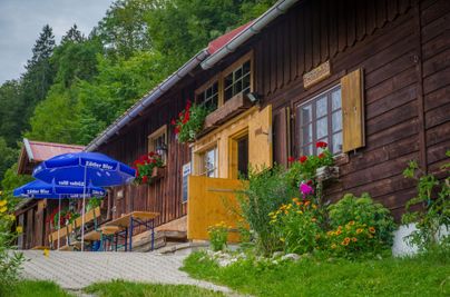 Eine gemütliche Berghütte mit blühenden Blumen und stilvollen Sonnenschirmen. Der Eingangsbereich ist einladend und von grünem Gras umgeben.