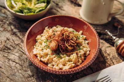 Ein appetitliches Gericht aus Reis mit gebratenen Zwiebeln und frischen Kräutern in einer tiefen Schale. Im Hintergrund sieht man eine kleine Schüssel mit Salat.