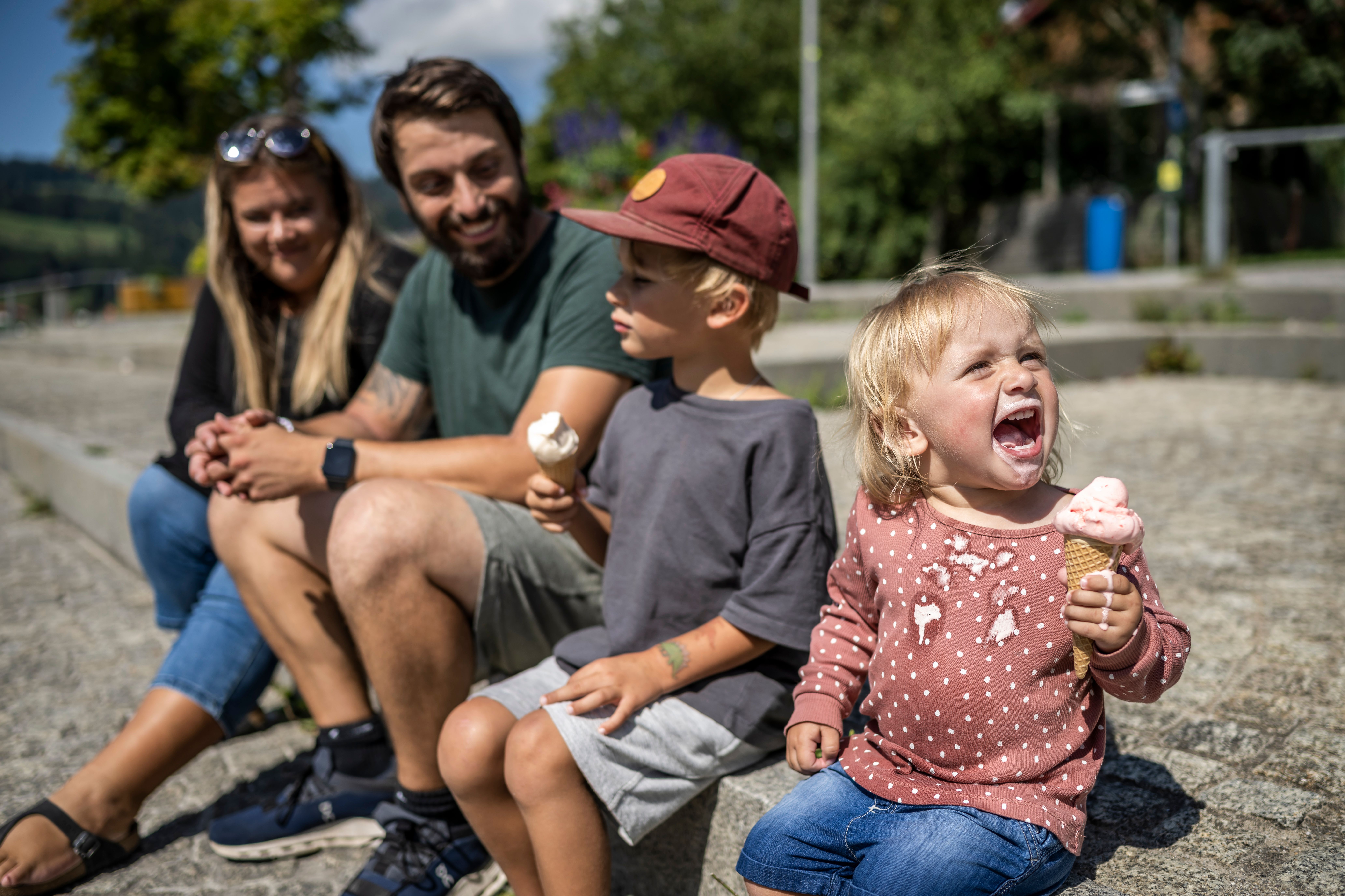 Eine Familie mit Mama, Papa und zwei Kindern sitzen an der Alpsee Promenade. Die zwei Kinder essen eine Kugel Eis auf der Waffel.