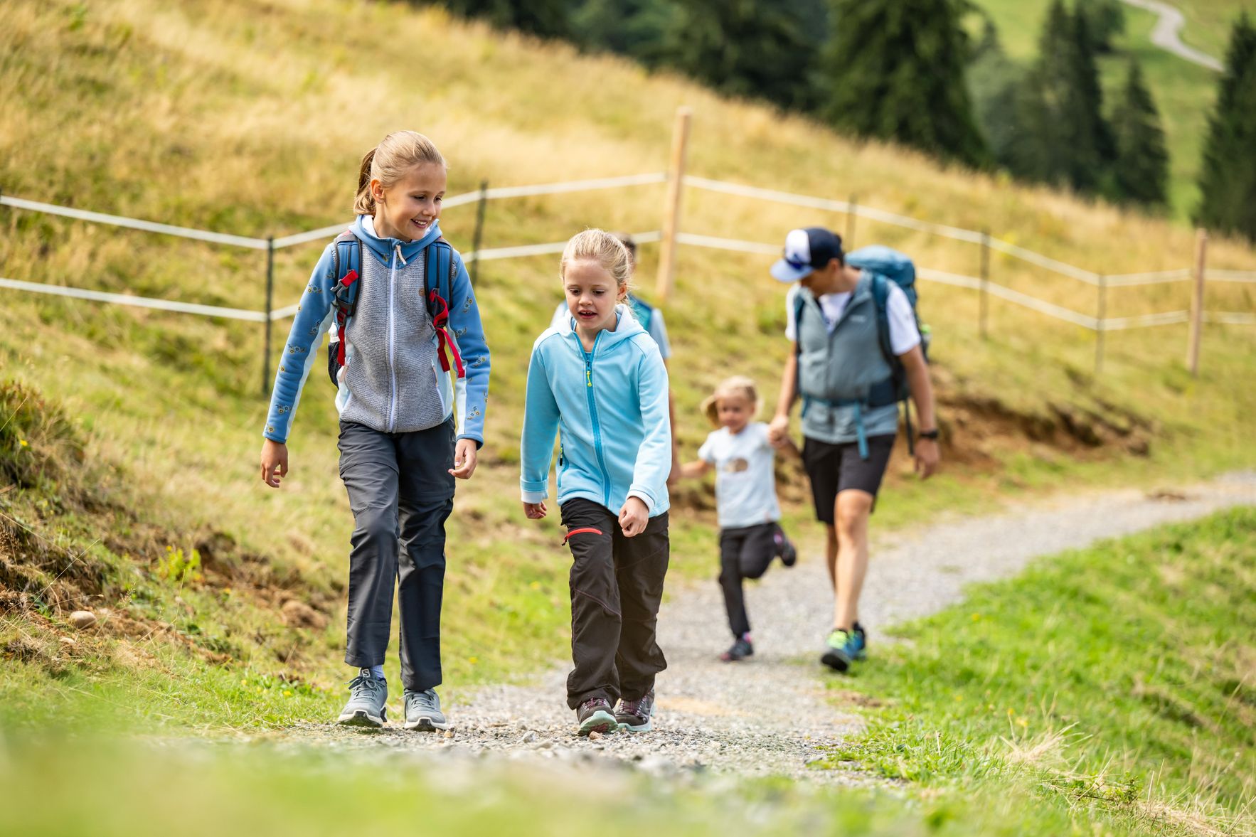 Eine Familie geht auf einem Weg bei Immenstadt. Es ist sonnig. Die Kinder sind fröhlich und tragen Rucksäcke.