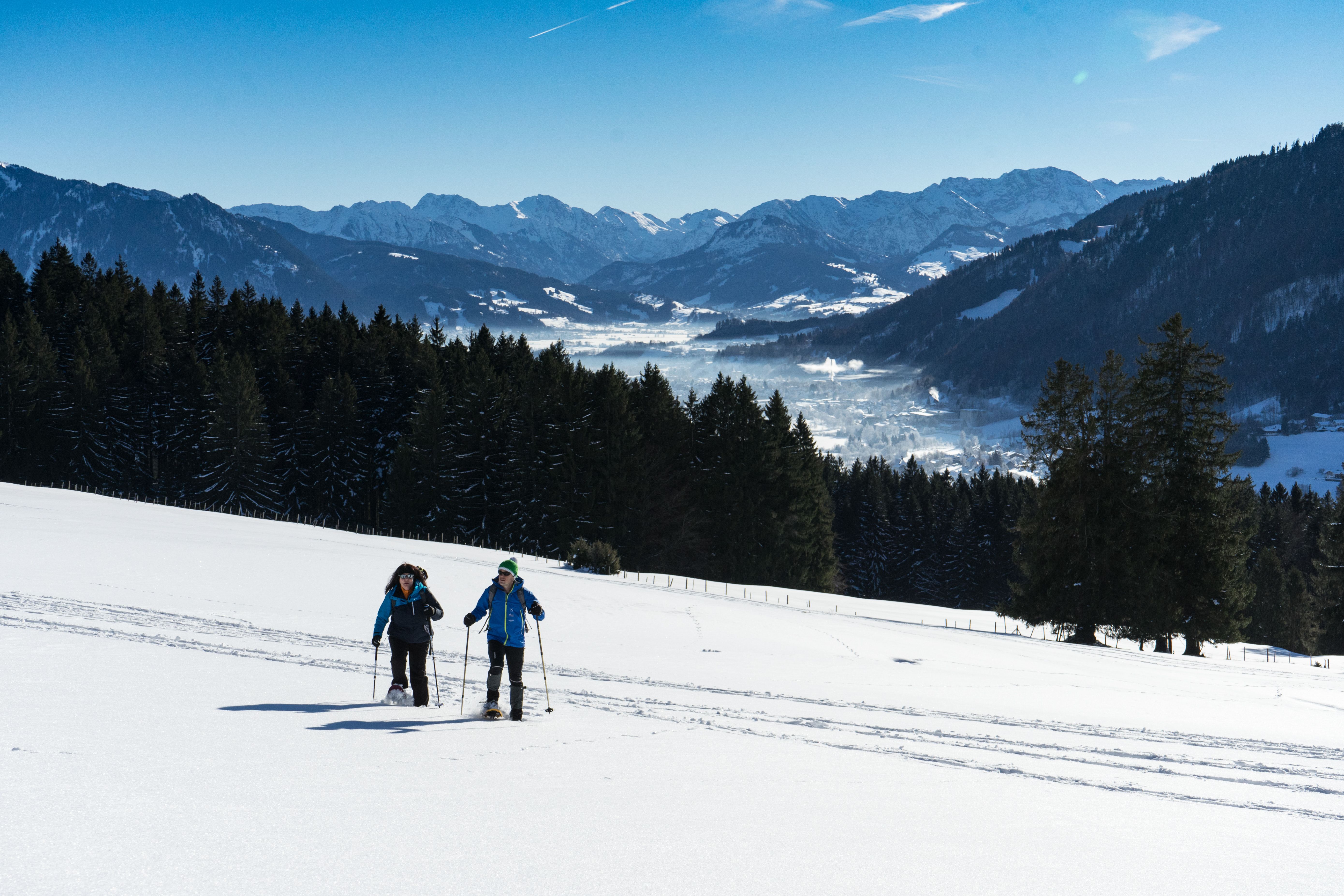 Zwei Schneeschuhwanderer während des leichten Anstiegs in Richtung Siedelalpe. Von hier aus kann man über Immenstadt und den Alpsee sowie weit in die schneebedeckten Alpen blicken.