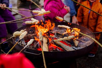 Mehrere Personen halten Stockbrot in das Feuer in der Feuerschale.