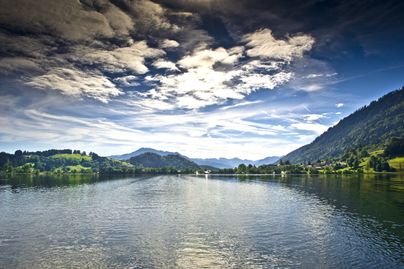Der Große Alpsee im Vordergrund, im Hintergrund sind der Bühler Hafen, der Grünten und die Allgäuer Hochalpen zu sehen.