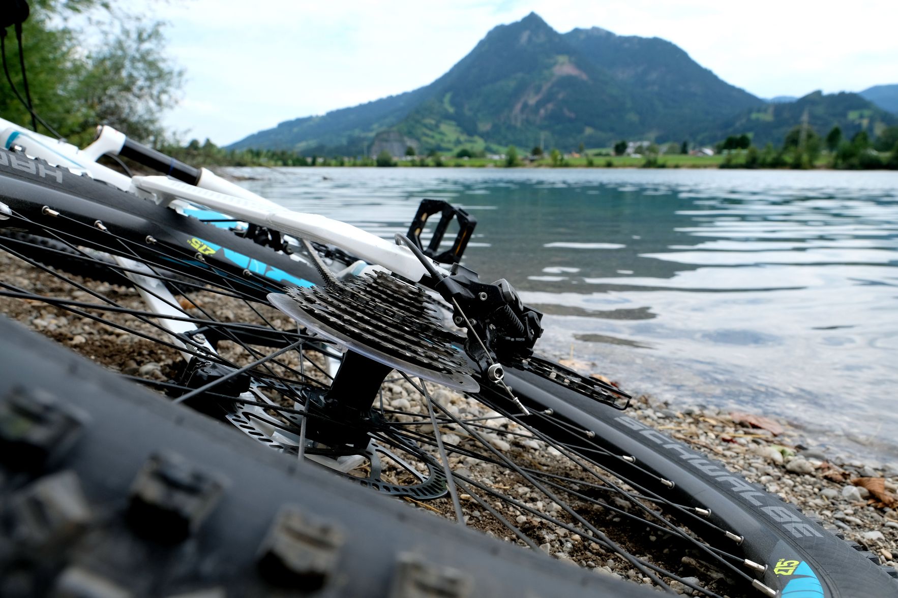 Ein weißes Fahrrad liegt am Ufer eines Sees. Im Hintergrund liegt der Grünten.