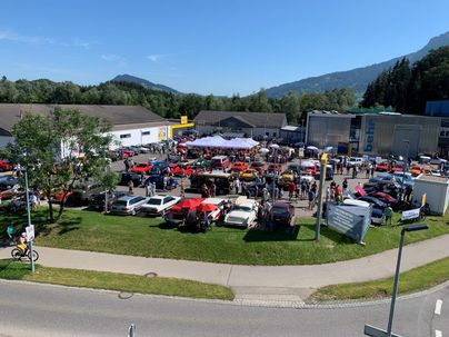 Eine große Versammlung von Oldtimer-Autos auf einem Parkplatz. Viele Menschen genießen die Veranstaltung bei schönem Wetter.