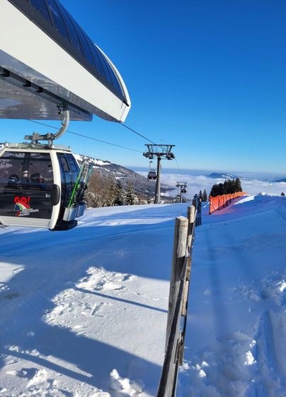 Eine Skiliftanlage mit schneebedeckten Pisten und strahlend blauem Himmel. In der Ferne sind weitere Lifte und schneebedeckte Bäume sichtbar.