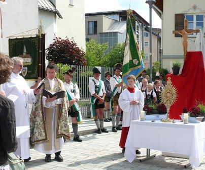 Eine religiöse Zeremonie im Freien mit Priestern und traditionell gekleideten Menschen. Auf einem Tisch stehen liturgische Gegenstände und eine große Flagge.