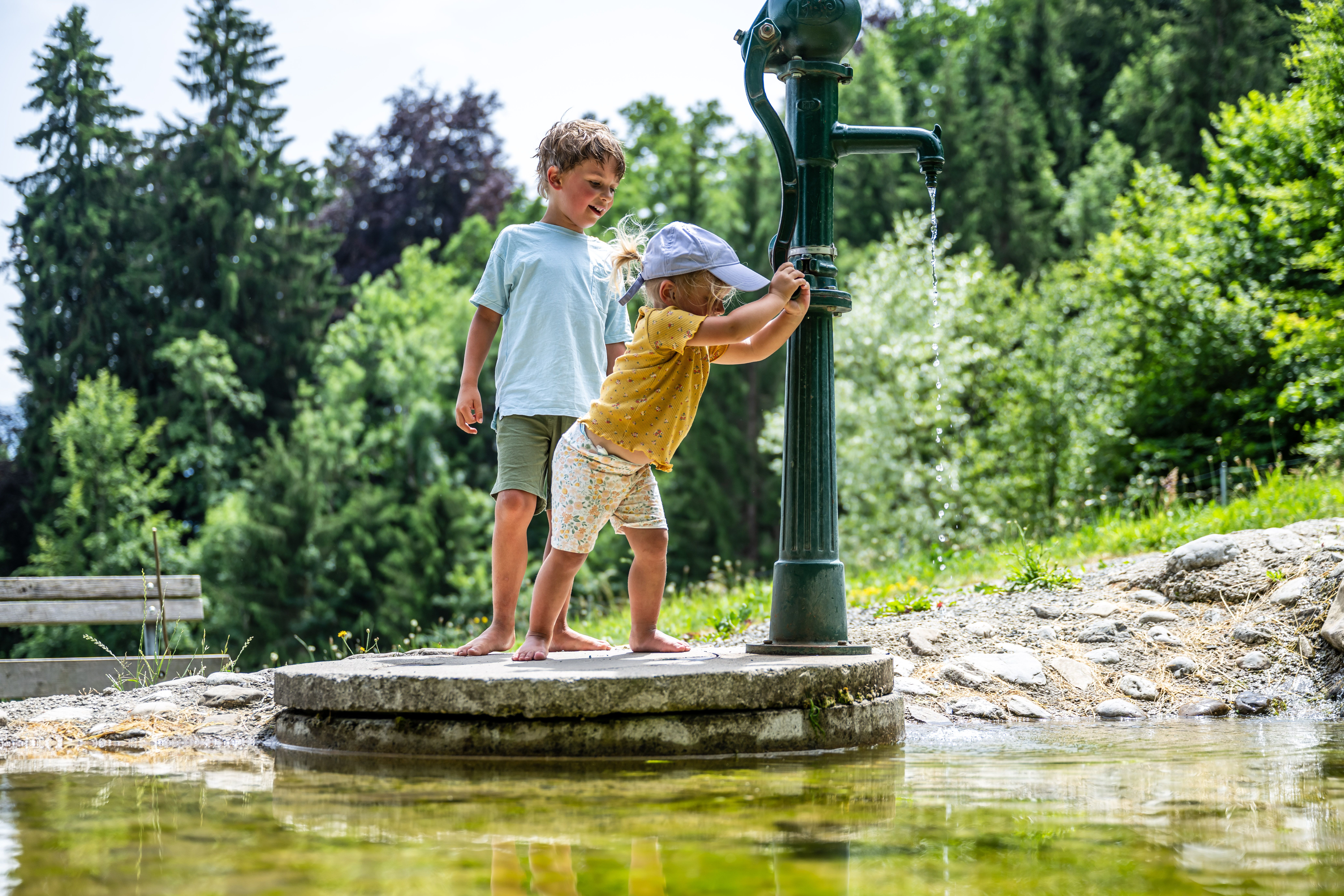 Ein Junge und ein Mädchen spielen auf dem Wasserspielplatz in Blaichach mit einem Brunnen.