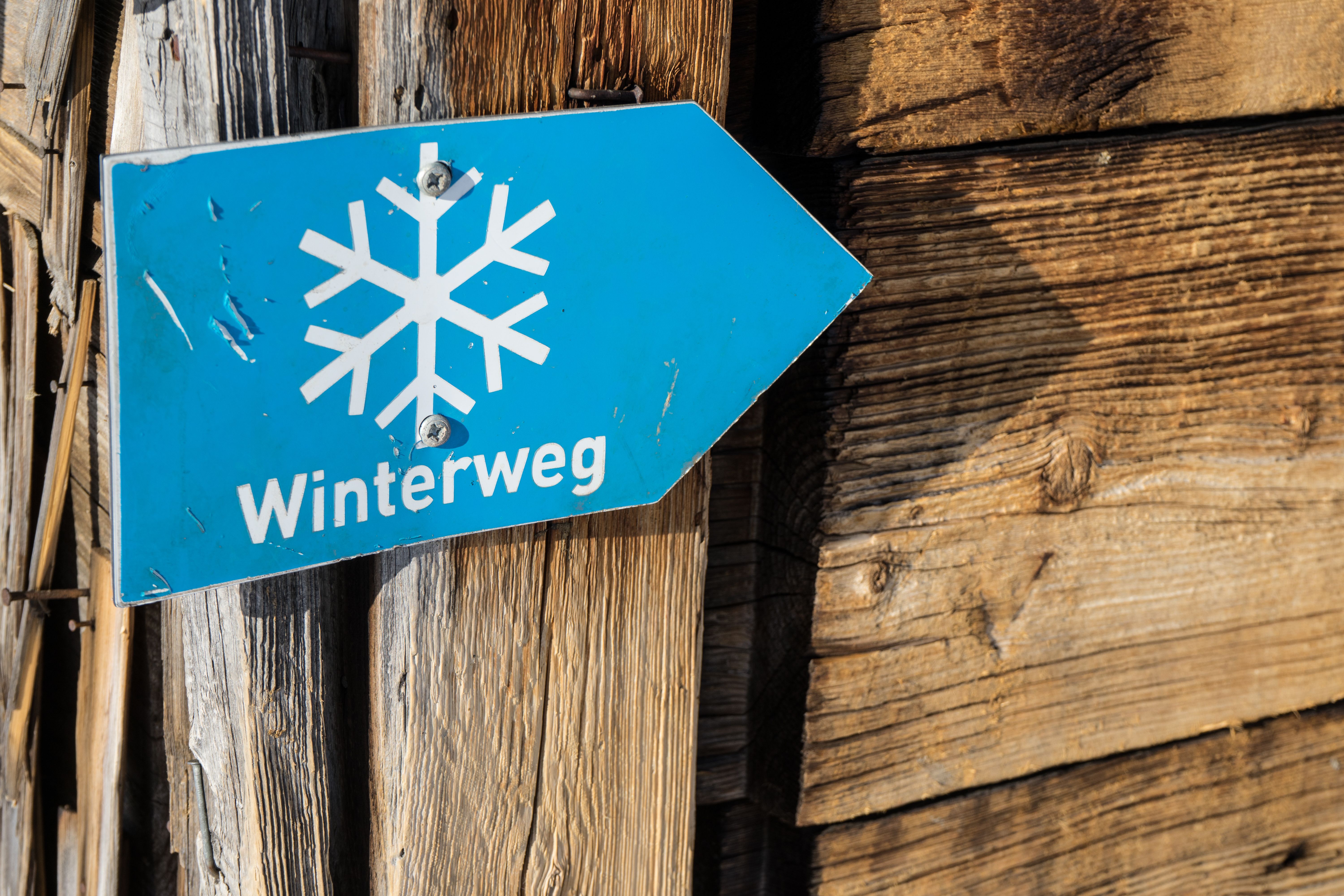 Ein Schild "Winterweg" ist auf eine Wand an eine Holzhütte geschraubt. Das Brauereidorf Rettenberg bietet die perfekte Ausgangslage für verschiedene Winteraktivitäten.