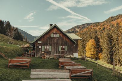 Eine charmante Holzhütte umgeben von Bergen und Bäumen. Der Herbst zeigt sich in schönen Farben.