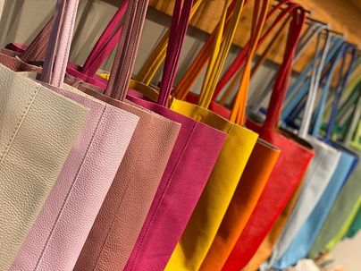 Eine Reihe bunter Einkaufsbeutel hängt an einer Wand. Die Taschen sind in verschiedenen Farben, darunter Rosa, Gelb, Orange und Blau.