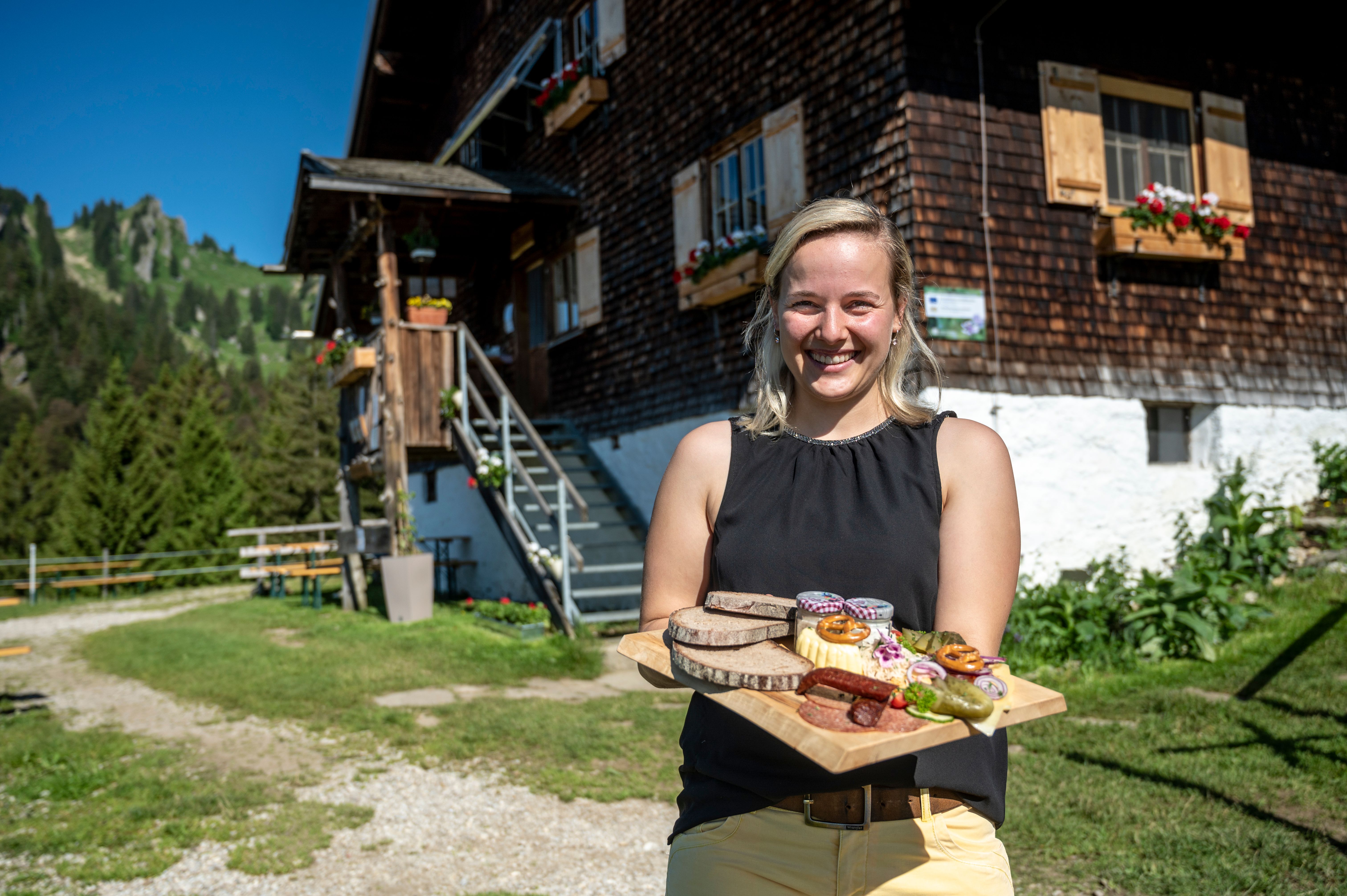 Hüttenwirtin Sofia Berchtold begrüßt ihre Gäste mit einer Brotzeitplatte auf der Alpe Vorder Krumbach im Gunzesrieder Tal mitten im Naturpark Nagelfluhkette.