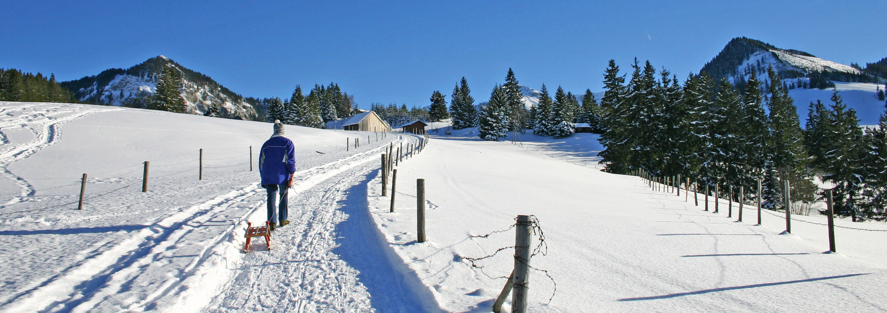 Ein Mann ist mit seinem Rodel auf dem schneebedeckten Winterwanderweg unterwegs zum Sonthofener Hof.