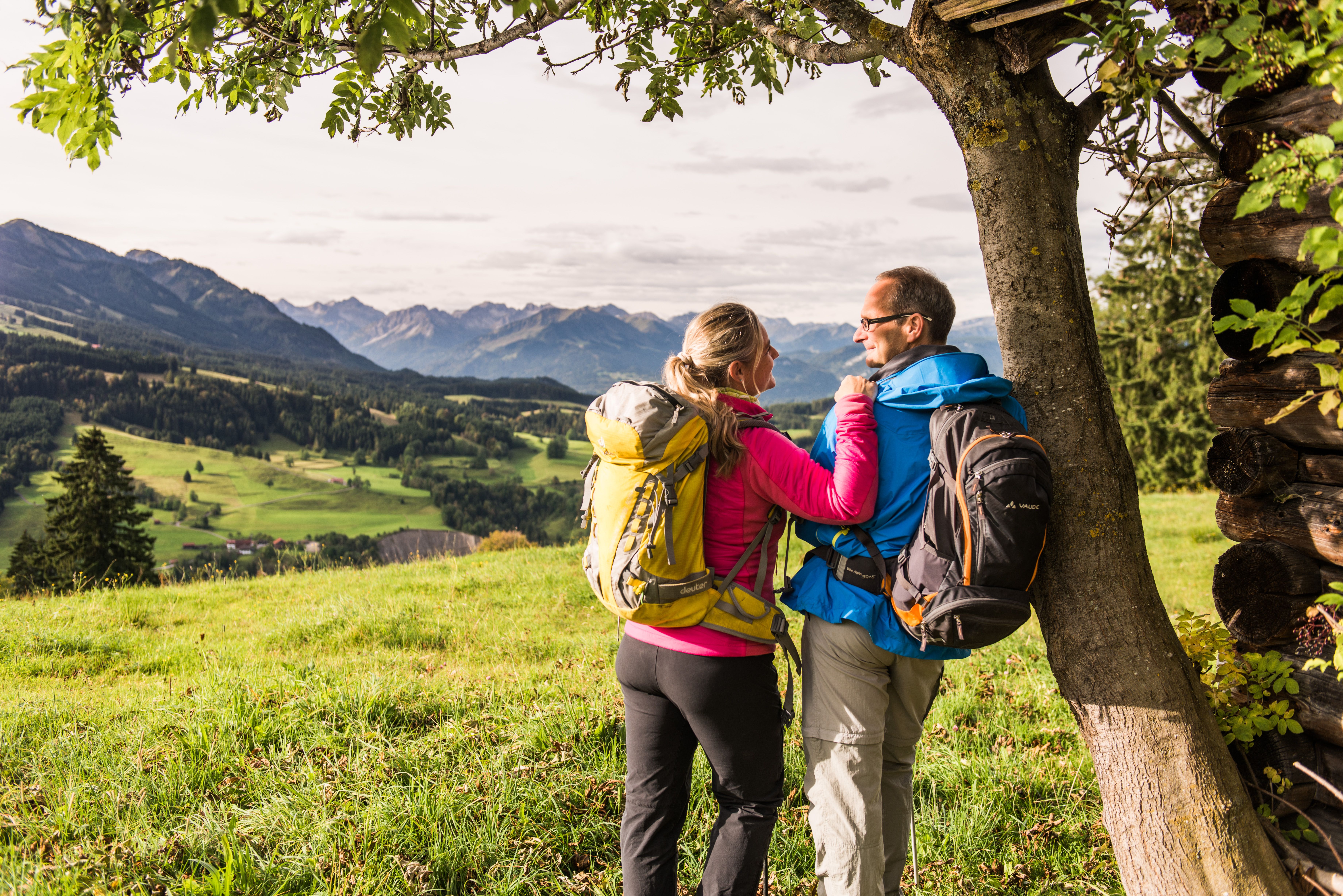 Zwei Wanderer lehnen in Wanderkleidung und mit Rucksäcken an einen Baum in Sonthofen.