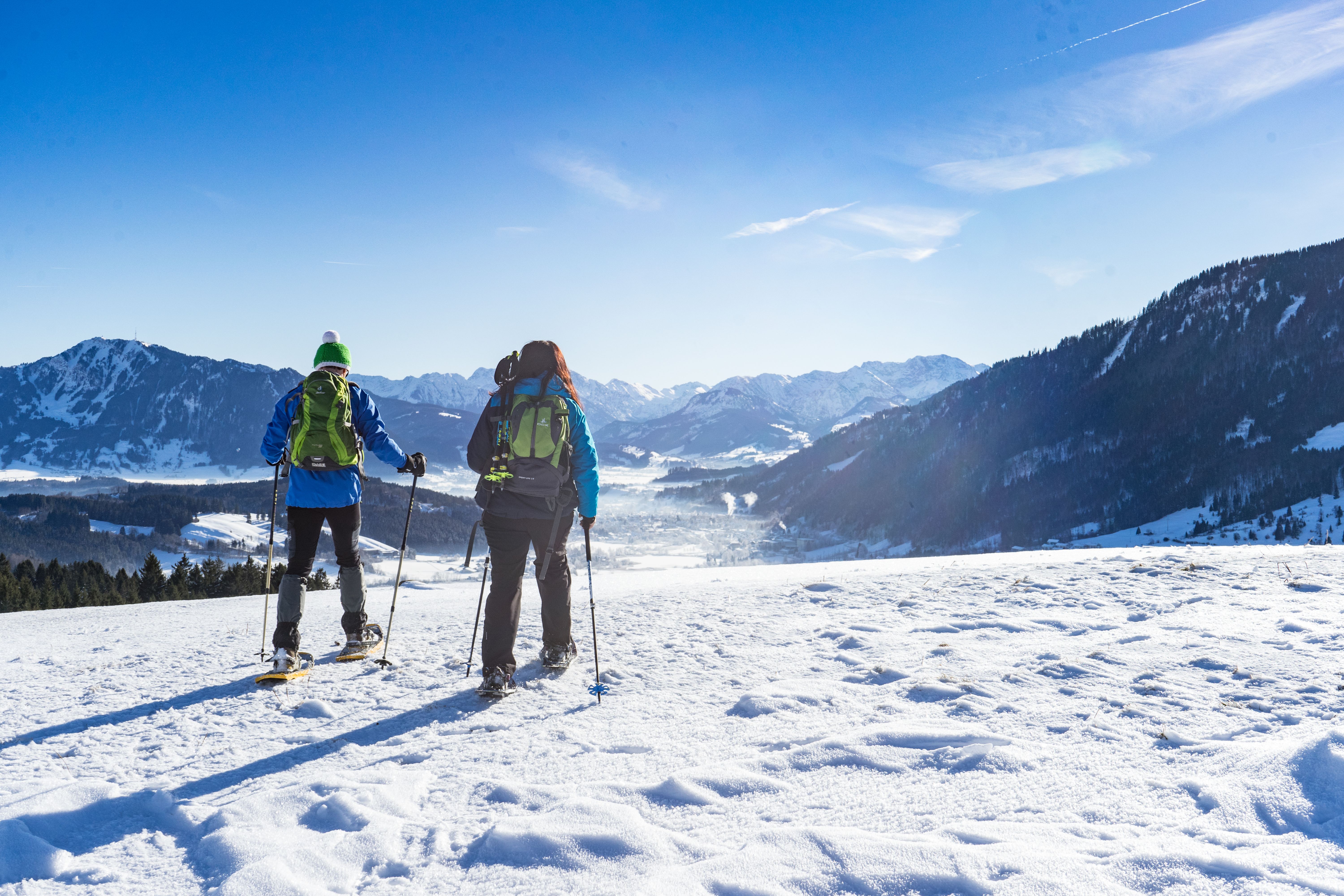 Zwei Schneeschuhwanderer laufen über Immenstadt, vor Ihnen erstreckt sich ein weiter Blick über das winterliche Immenstadt, den Grünten und die Allgäuer Alpen.