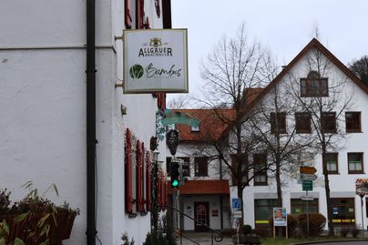 Ein Gebäude mit einem Schild, das das Restaurant "Augsburg" anzeigt. Im Hintergrund sind weitere Häuser und Bäume sichtbar.