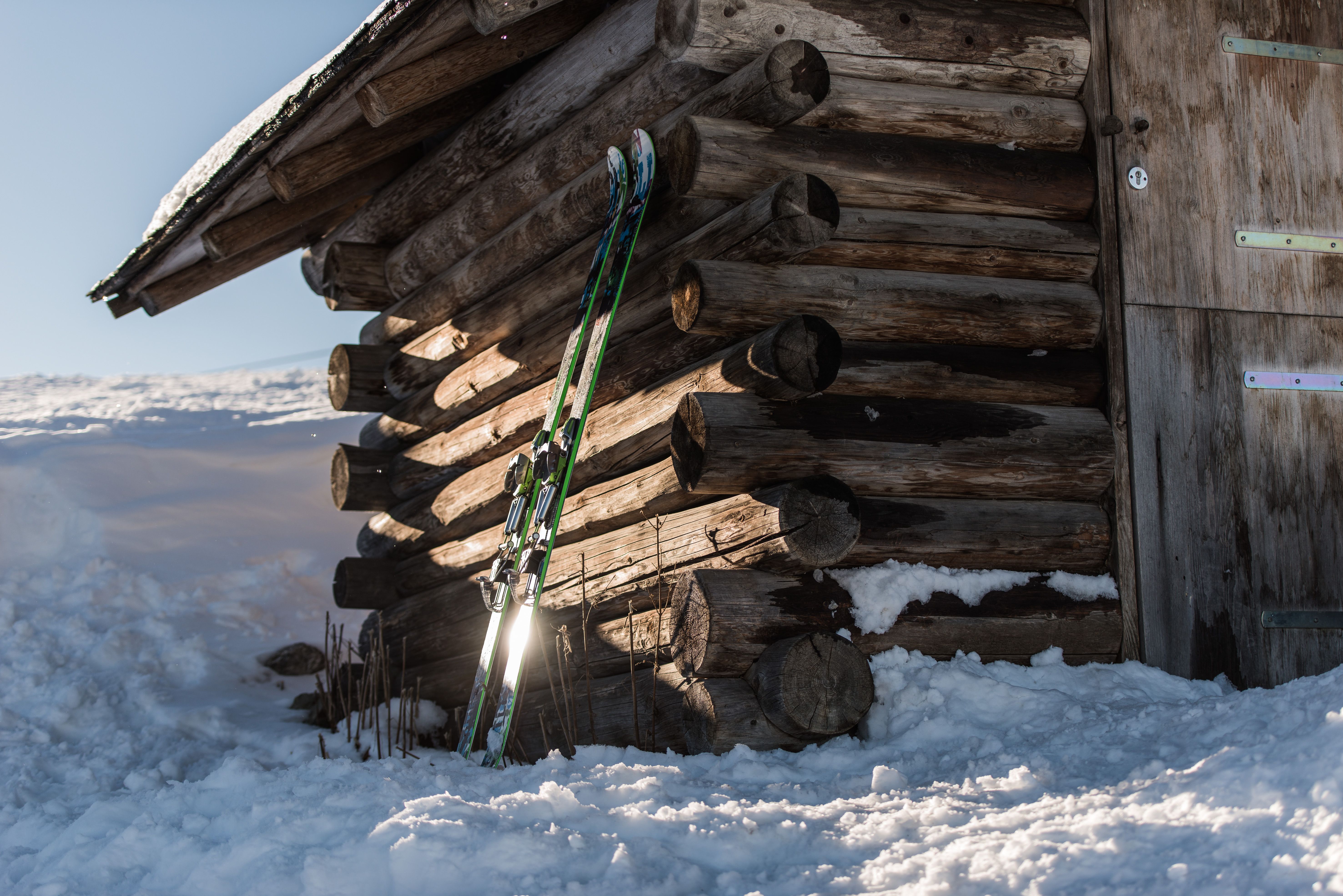 Ein Paar Tourenski lehnen im Winter an einer Holzhütte umringt von hohem Schnee.