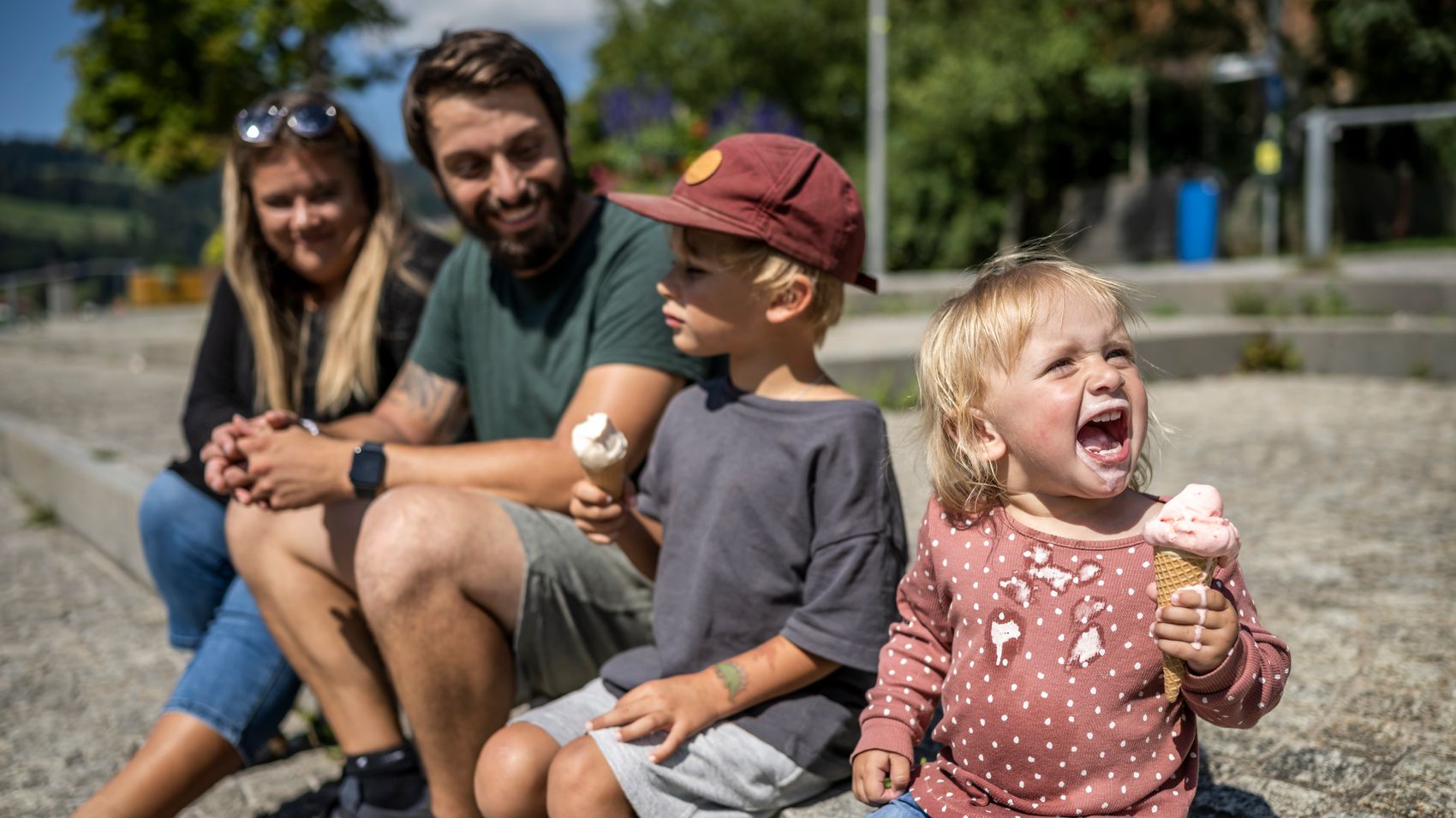 Eine Familie mit Mama, Papa und zwei Kindern sitzen an der Alpsee Promenade. Die zwei Kinder essen eine Kugel Eis auf der Waffel.