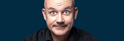Ein Mann mit kahlrasiertem Kopf lächelt freundlich in die Kamera. Der Hintergrund ist einfarbig und dunkelblau.
