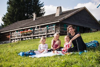 Ein Vater sitz mit seinen drei Mädchen auf einer Picknickdecke vor der Höfle Alpe am Bergbauernmuseum in Diepolz.