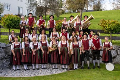Eine Gruppe von Musikern in traditionellen Trachten steht auf einer Wiese. Sie spielen verschiedene Blasinstrumente und lächeln in die Kamera.