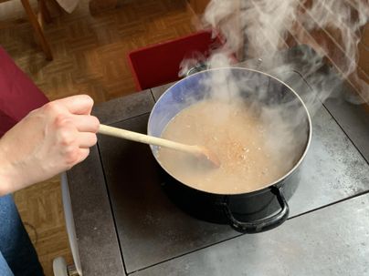 Ein Topf mit dampfender Brühe auf dem Herd. Eine Hand rührt mit einem Holzlöffel in der Suppe.
