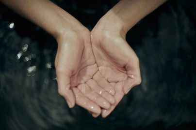 Hände halten frisches Wasser in einer ruhigen Umgebung. Das Wasser spiegelt sich sanft in den Händen.