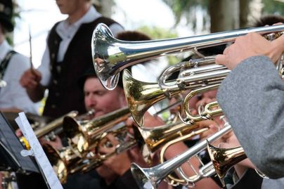 Eine Blaskapelle spielt Musik im Freien. Im Vordergrund sind mehrere Trompeten und Musiker zu sehen.
