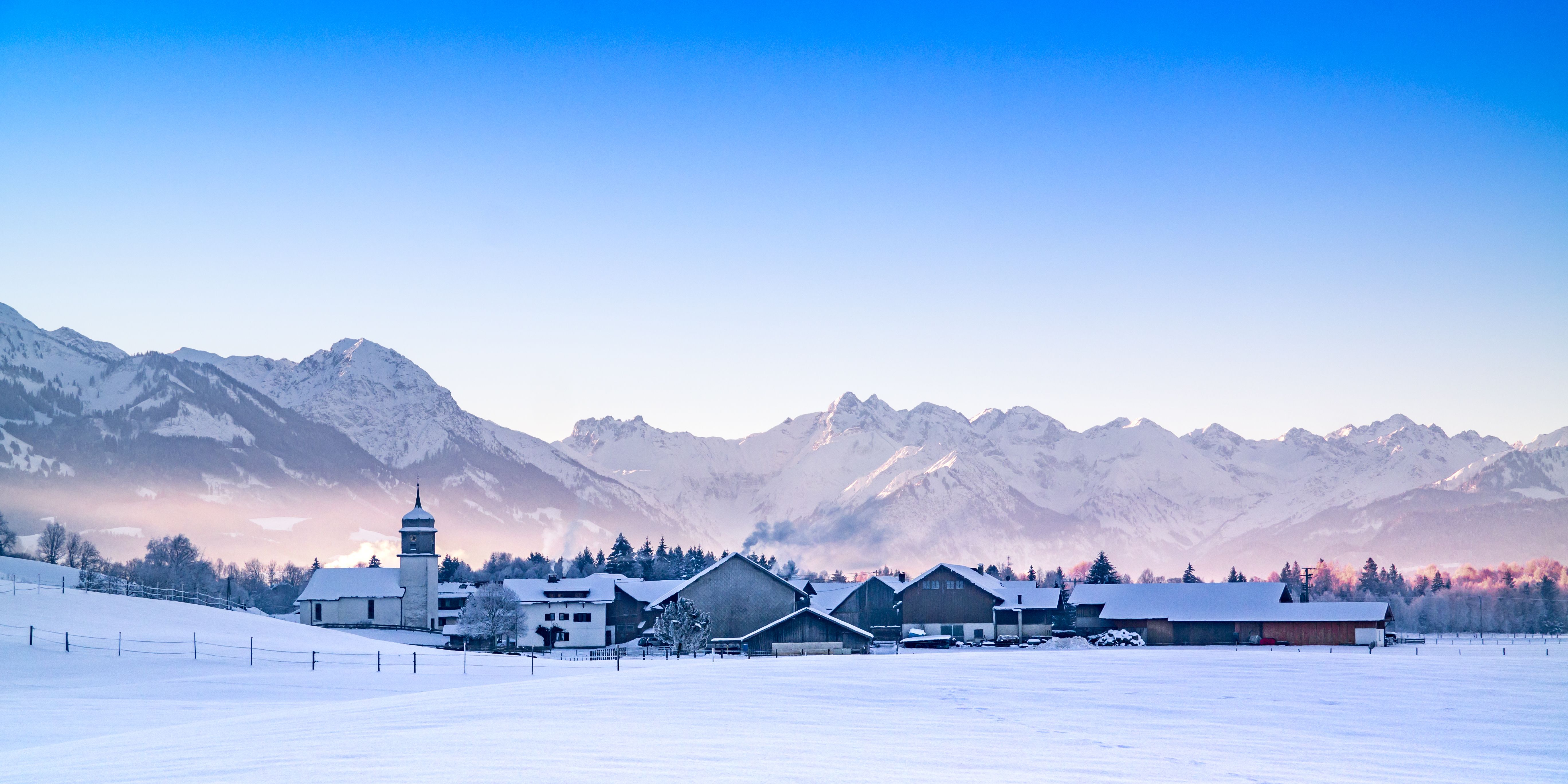 Der Burgberger Ortsteil Agathazell im Winter mit schneebedeckten Dächern und wunderschönem Bergpanorama im Hintergrund.