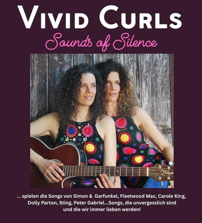 Zwei Frauen stehen neben einem vintage grünen Auto und halten eine akustische Gitarre. Im Hintergrund ist eine weite Wiese zu sehen.
