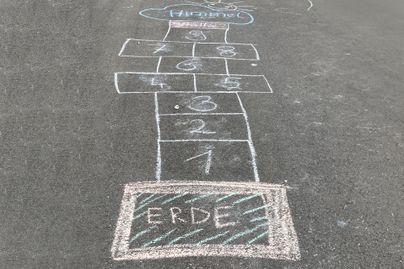 Ein selbstgemaltes Hüpfspiel auf dem Boden mit Zahlen von 1 bis 8. Am Ende steht das Wort "ERDE" in großen Buchstaben.