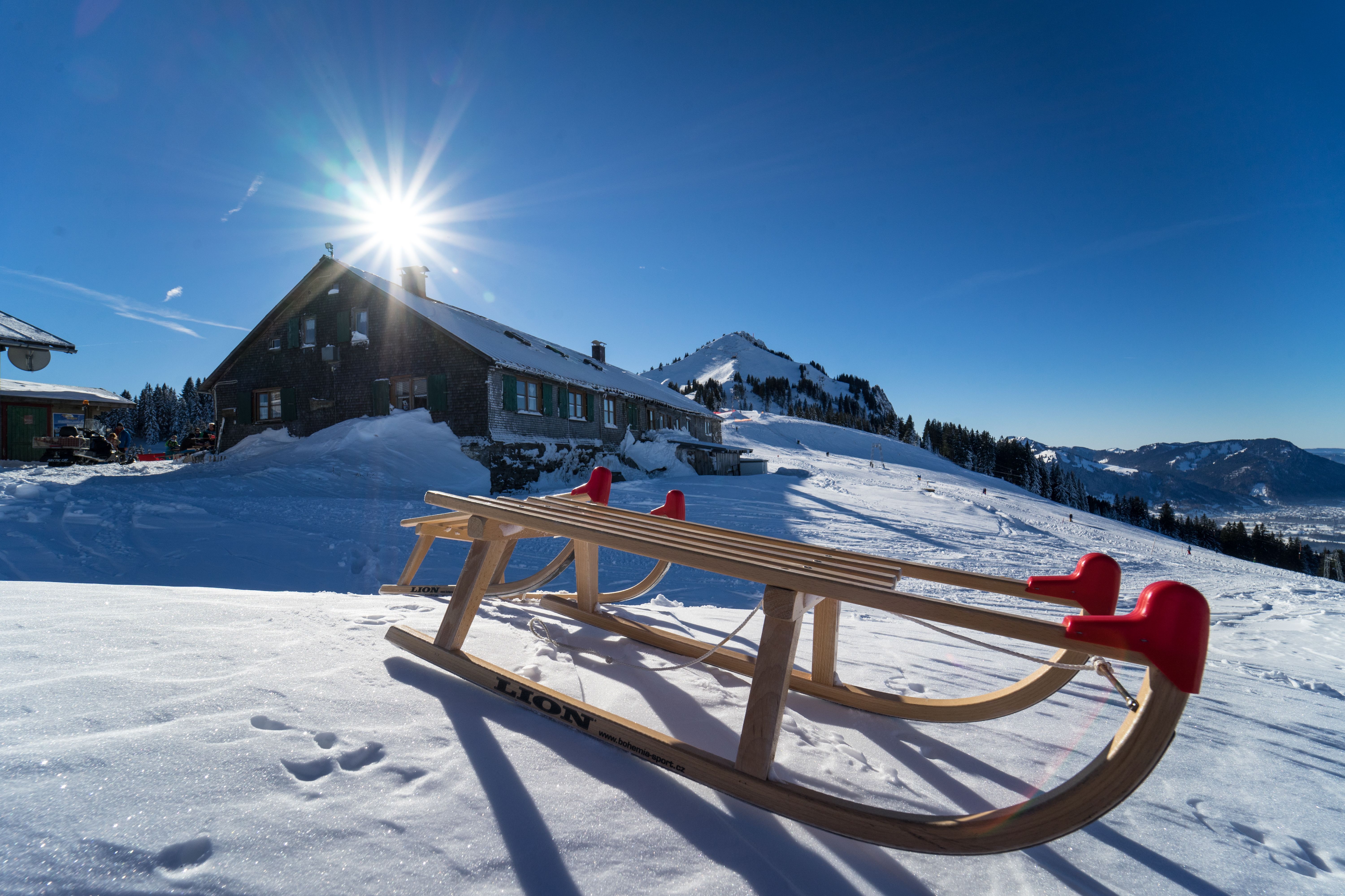 Zwei Schlitten liegen im Winter vor der Grüntenhütte in Rettenberg. Die Grüntenhütte liegt auf 1.477 Metern in traumhafter Lage unterhalb des Grüntengipfels. Von Kranzegg erreicht man die Einkehrhütte über einen gut ausgebauten Alpweg oder einen idyllischen Wald- und Wiesenweg
